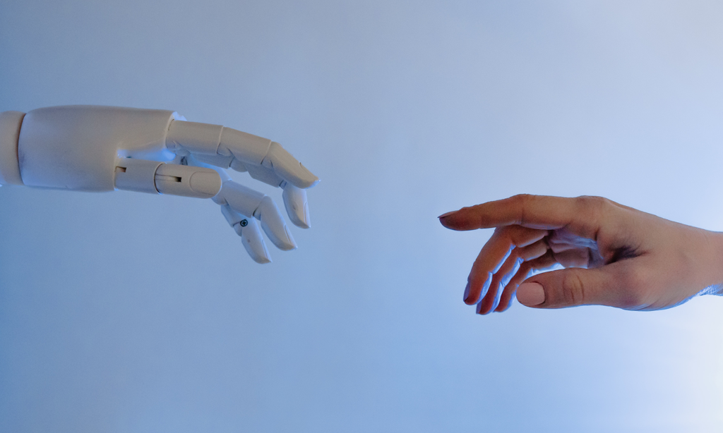 GPT. Imagem de fundo azul claro, no lado esquerdo uma mão de robô e no lado direito uma mão humana e feminina, as duas mãos perto uma da outra quase se tocando.